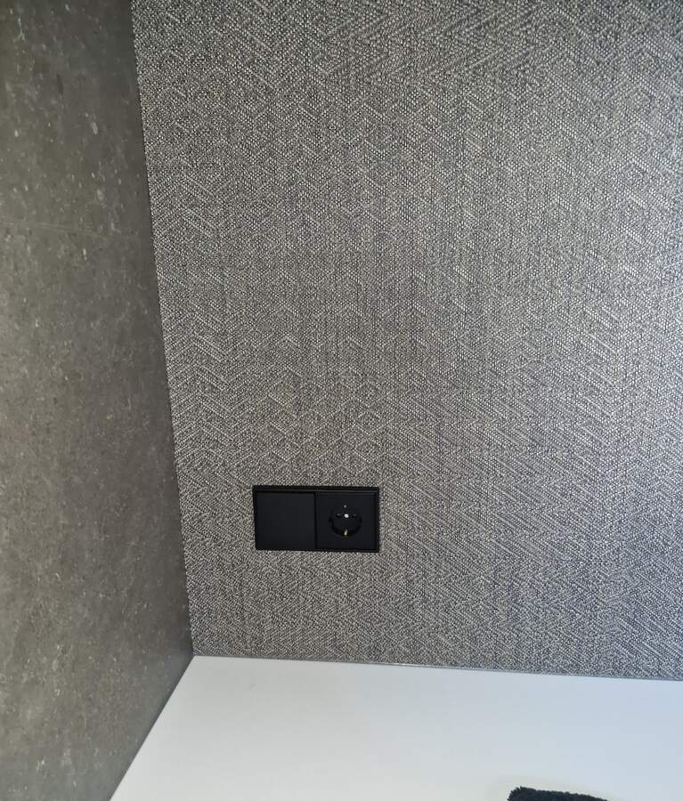 Schwarze Schalter- und Steckdosenkombination an einer strukturierten Wand